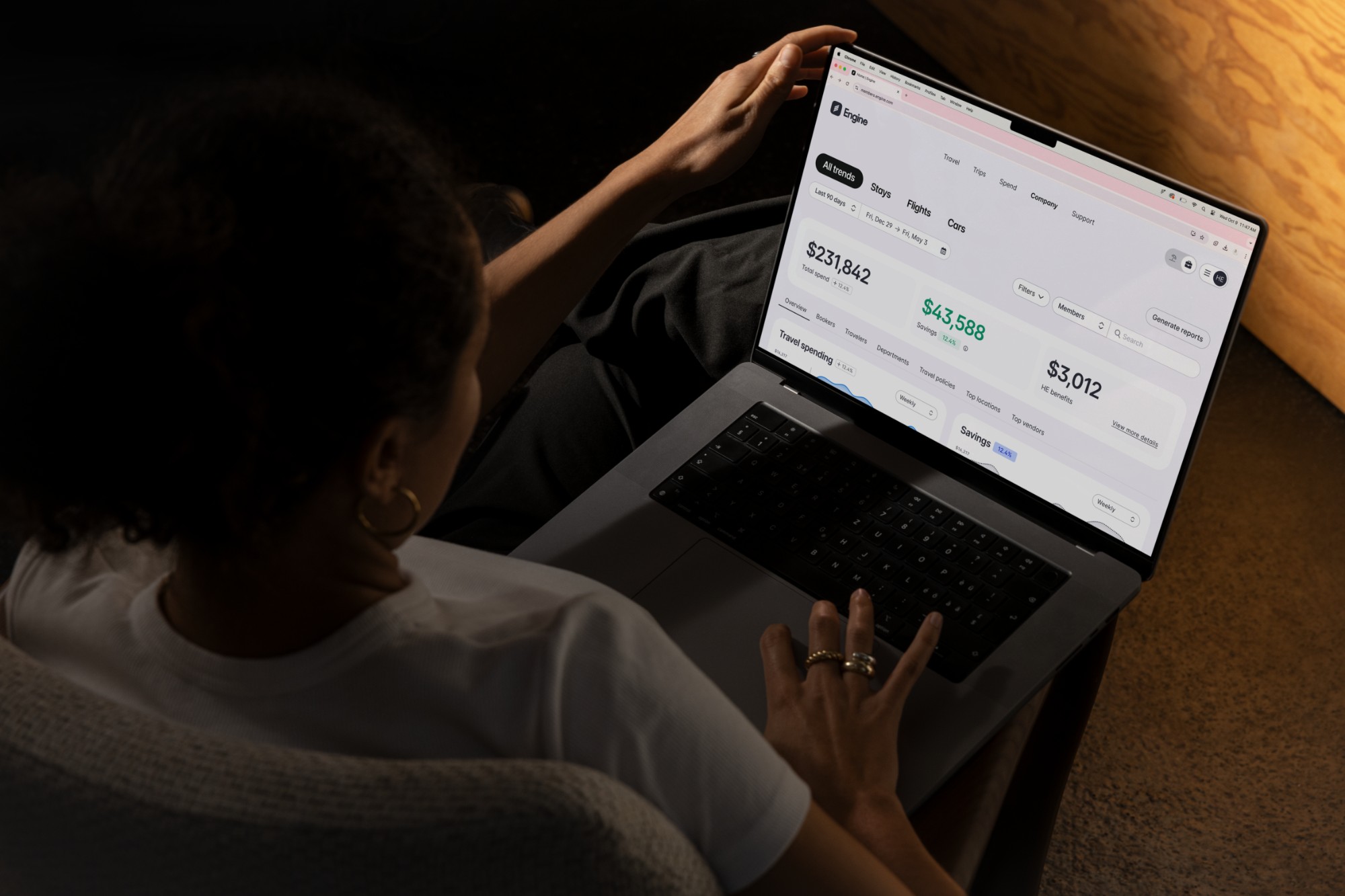 A traveler reviewing Engine's spend and savings dashboard on a laptop, showing $231,842 total spend and $43,588 in savings