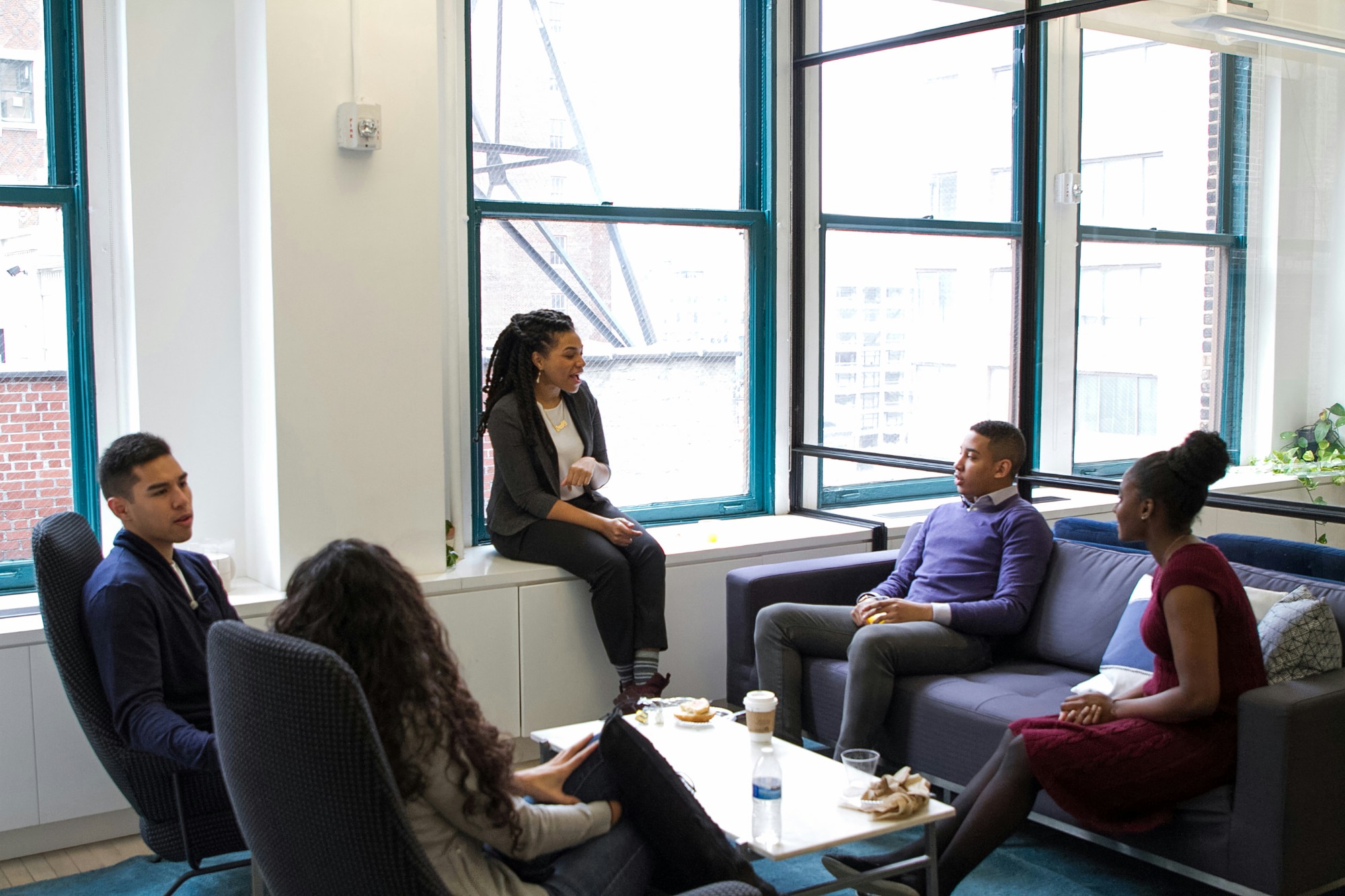 A group of employees in an office lounge discussing in front of a window