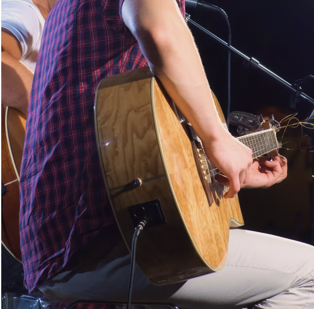A man playing a guitar with a plaid shirt on.